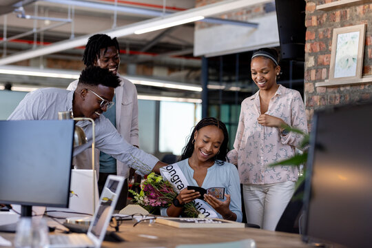 Celebrating success, diverse colleagues congratulating woman with flowers at office gathering