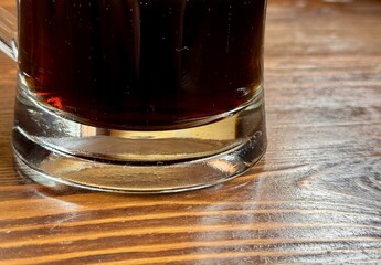 An unfinished transparent glass mug with dark beer and foam on the bar in an elite pub