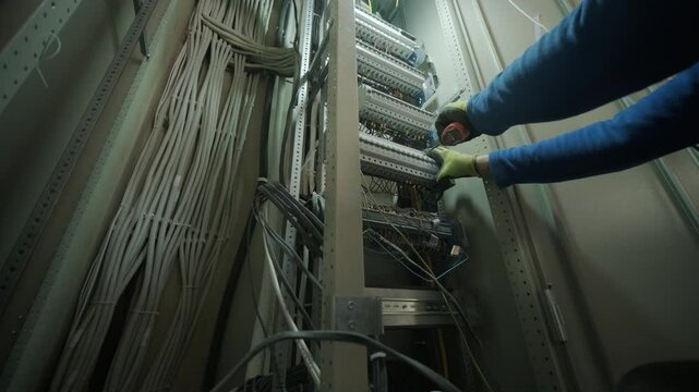 Electrician installing or repairing wiring in electrical control cabinet