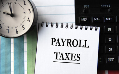 PAYROLL TAXES - words in a white notebook with an alarm clock and calculator in the background