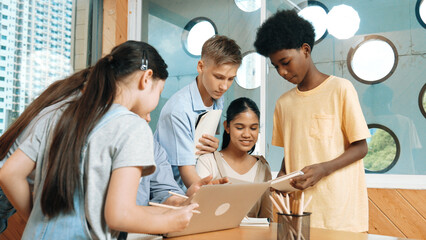 Caucasian teacher giving comment or advise student while smart bot pointing at laptop screen at classroom. Diverse student taking a note while teacher teach lesson while using computer. Edification.