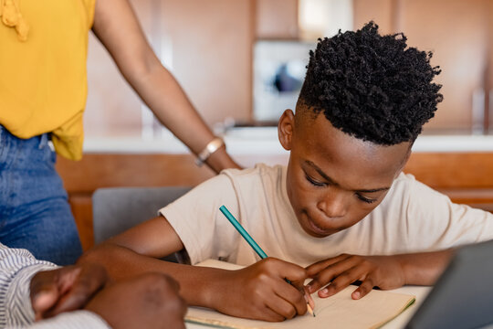 African American boy writing in notebook at home, concentrating on homework