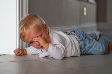 Fototapeta premium Toddler's Emotional Outburst: a small child weeps while lying on the floor, conveying sadness and frustration.