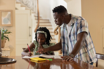 Helping daughter with homework, African American father and child at kitchen table