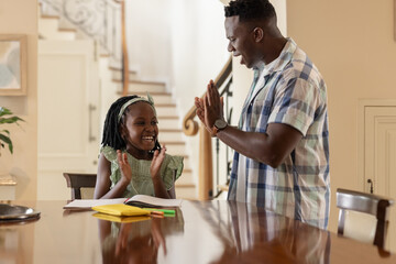 African American father and daughter clapping hands together while studying at home