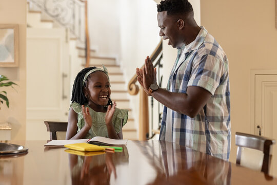 African American father and daughter clapping hands together while studying at home