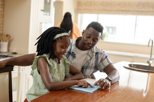 Helping daughter with homework, African American father at kitchen table smiling