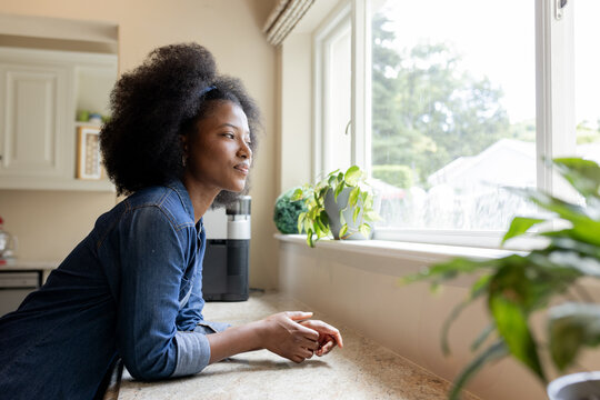 African American woman gazing out window at home, enjoying peaceful moment, copy space