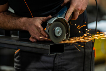 Technicien en atelier en train de disquer une barre en métal avec une meuleuse, produisant des étincelles.