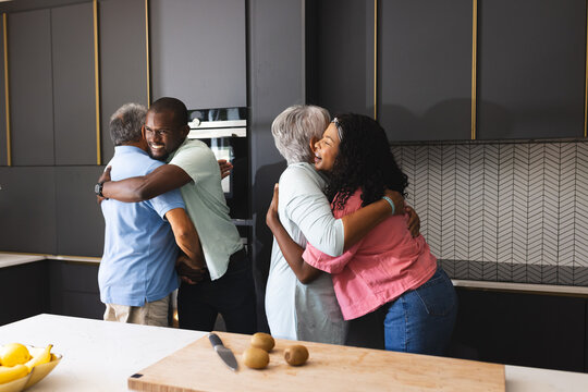 Multigenerational family gathering in kitchen, three generations sharing warm hugs and laughter, at