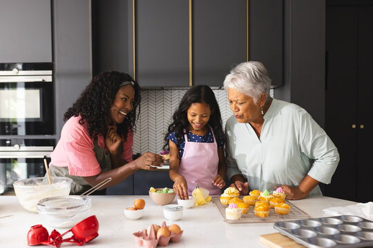 Three happy generations baking , smiling and decorating cupcakes in modern kitchen, at home