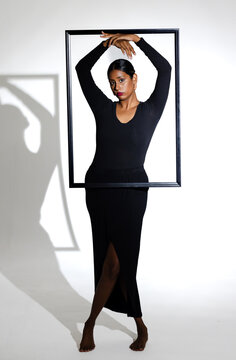 Model posing creatively with black frame, wearing elegant black dress