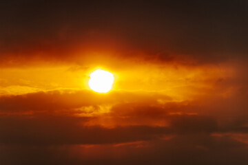 Obraz premium A partial solar eclipse glows through dramatic red-orange clouds, casting an intense and surreal light in a dark sky. Includes ample copy space.