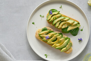 Close up view of avocado toast. Open sandwich with avocado slices served on a white plate against grey background. Top view      