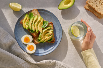 Young woman hand holding fresh lime juice and having healthy avocado and egg breakfast. Creative...