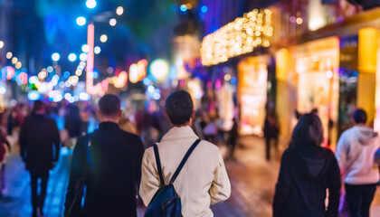 Fototapeta premium Personas variadas caminando con desenfoque de movimiento por por la noche una calle de ciudad iluminada con ambiente cálido