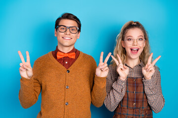 Young couple in retro clothing style smiling and showing peace gestures over a blue background