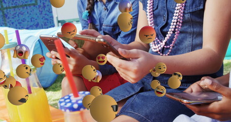 Using smartphones outdoors, children surrounded by floating emojis, embracing technology