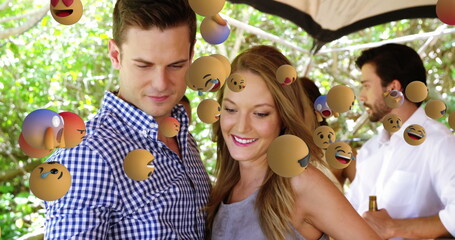 Couple enjoying outdoor party surrounded by floating emoji symbols, smiling together