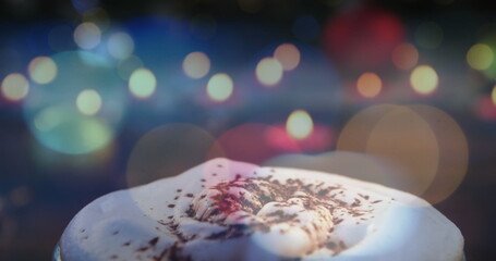 Hot chocolate with whipped cream and chocolate shavings, holiday lights glowing