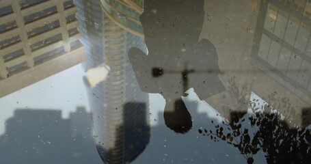 Reflection of person in city puddle with skyscrapers and tree branches visible