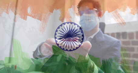 Composition of businessman wearing face mask disinfecting his hands in office over indian flag
