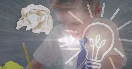 Image of lit light bulb over schoolboy writing in class in background