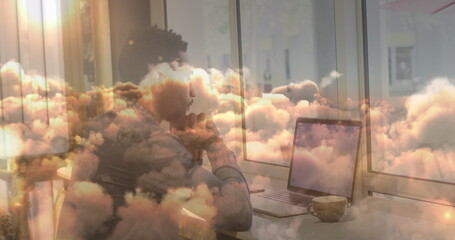 Image of businessman using laptop in office over moving clouds