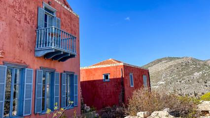 Rustic Greek House With Blue Shutters And Balcony In Mountain Village, Red Walls Under Bright Blue Sky, Taken In Greece During Summer, Ideal For Travel, Architecture, And Lifestyle Concepts