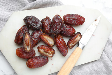 Many tasty dried dates, cutting board and knife on table, top view