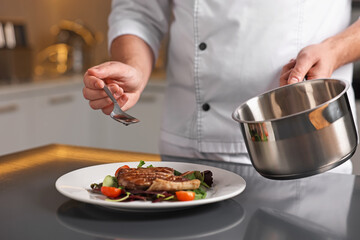 Professional chef adding sauce to delicious dish at table indoors, closeup