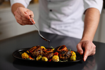 Professional chef adding sauce to delicious dish at table indoors, closeup