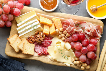 Different types of cut cheese and other snacks served with wine on gray textured table, flat lay