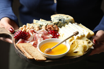 Woman holding board with different types of delicious cheese and other snacks, closeup