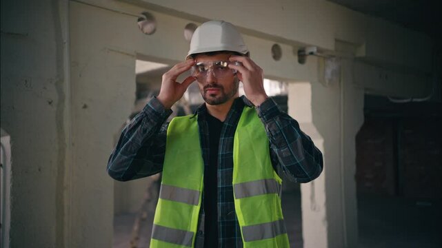Serious Caucasian guy mechanic man repairman employee putting on safety glasses in construction factory workwear engineer builder protect eyes male handyman wear gear manufacturing contractor building