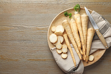 Parsley roots and knife on wooden table, top view. Space for text