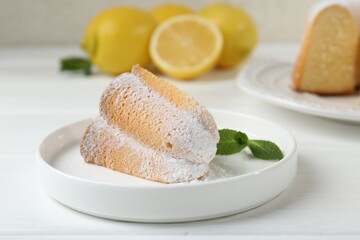 Piece of delicious lemon cake with powdered sugar and mint on white wooden table, closeup