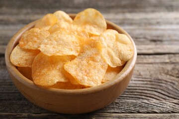 Tasty potato chips in bowl on wooden table, closeup