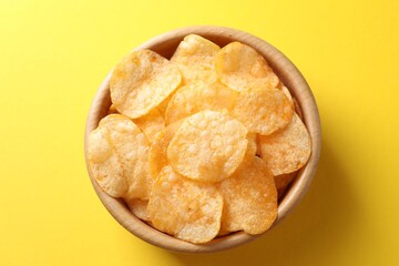 Tasty potato chips in bowl on yellow background, top view