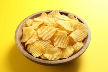 Tasty potato chips in bowl on yellow background, closeup