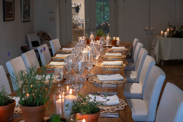 Untouched wooden dinner table served with glassware, silverware and candle decorations for gathering and celebration at a small cozy rustic winery restaurant, selective focus.