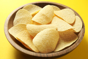 Tasty potato chips in bowl on yellow background, closeup
