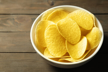 Tasty potato chips in bowl on wooden table, closeup. Space for text
