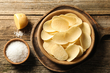Tasty chips, salt and raw potato on wooden table