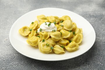 Tasty dumplings with green onion and sour cream on grey textured table, closeup