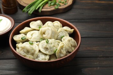Tasty dumplings with green onion and dill in bowl on wooden table, closeup
