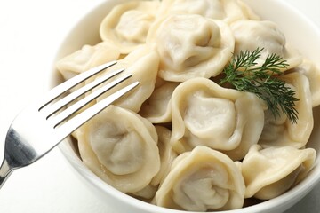 Tasty dumplings and dill in bowl on white table, closeup