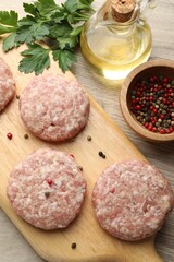 Many uncooked patties and spices on wooden table, flat lay
