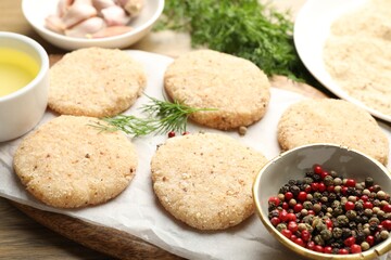 Many uncooked patties and spices on wooden table, closeup