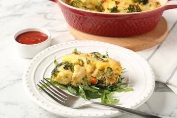 Tasty vegetable casserole, arugula and fork on white marble table, closeup
